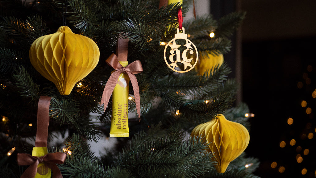Photo showing a close up of a Christmas tree with yellow and gold decorations including an Absolute Collagen sachet tied with a pink bow