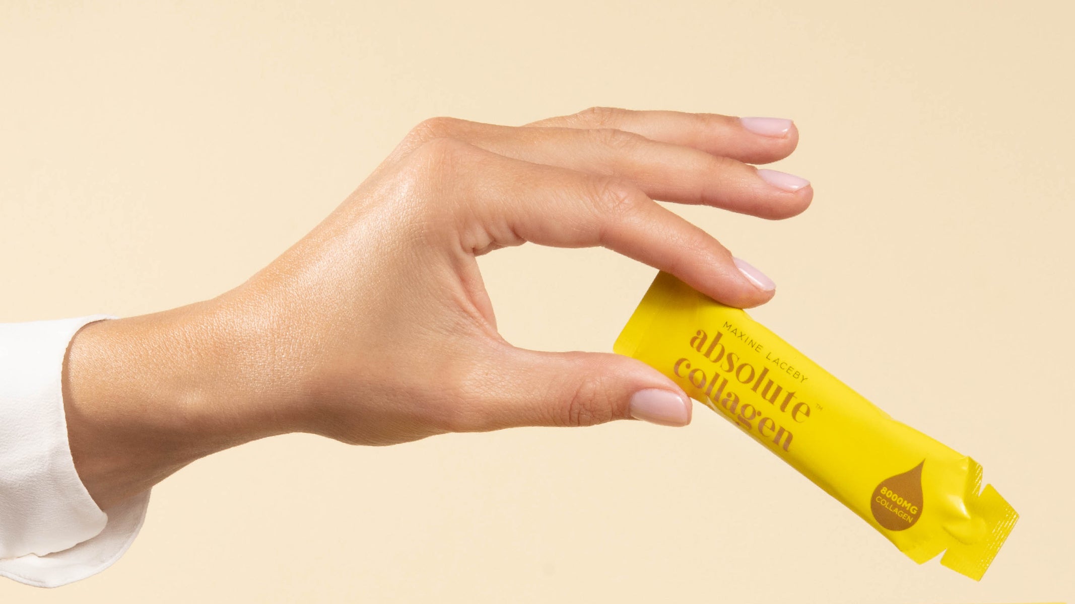 Photo showing a white woman's hand with beautiful fingernails holding up a sachet of Absolute Collagen