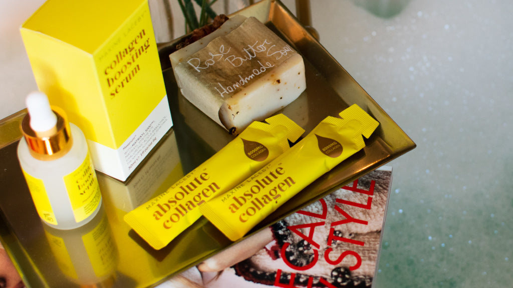 Photo showing a bottle of Maxerum and yellow Absolute Collagen sachets on a small tray with a bath full of bubbles in the backgound