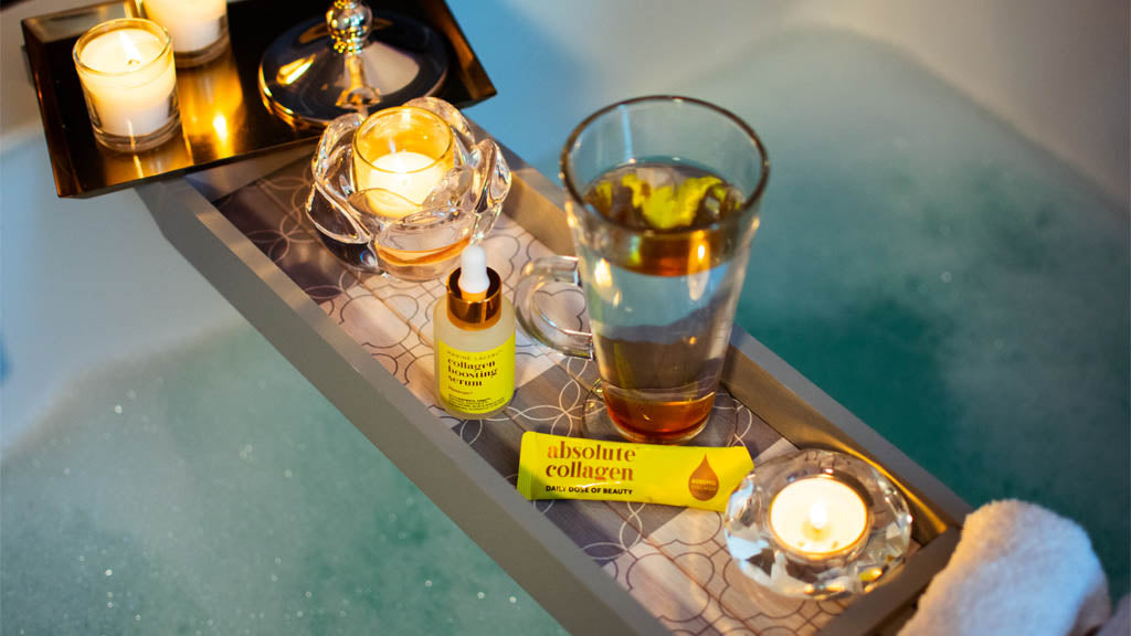 Photo showing a relaxing bubble bath with a wooden bath tray that contains a latte glass, candles, flannels, Maxerum and an Absolute Collagen sachet
