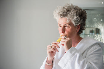 Photo of a white woman with short grey hair wearing a white dressing gown and taking a yellow Absolute Collagen sachet